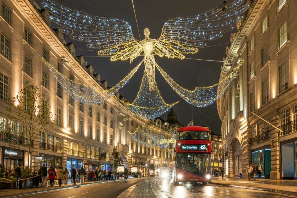 This image captures a vibrant street scene in the UK at night. Illuminated by festive lights, a large, winged figure made of twinkling bulbs stretches across the street above a classic red double - decker bus. The surrounding buildings are lit up, and people are walking along the sidewalks, adding to the bustling atmosphere. On LinkedIn UK, effective B2B marketing strategies can incorporate visuals like this. You can create content that showcases the energy and innovation of the UK business environment, perhaps relating the festive and dynamic street scene to the forward - thinking nature of your company. Share stories about how your products or services fit into the modern, vibrant UK landscape. Engage with industry influencers and participate in relevant groups to increase your brand's visibility and establish your business as a key player in the B2B market.